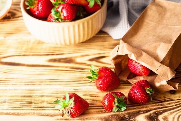 Frische rote Erdbeeren in der Schüssel und Papiertüte im hölzernen Hintergrund Rustikaler Stil