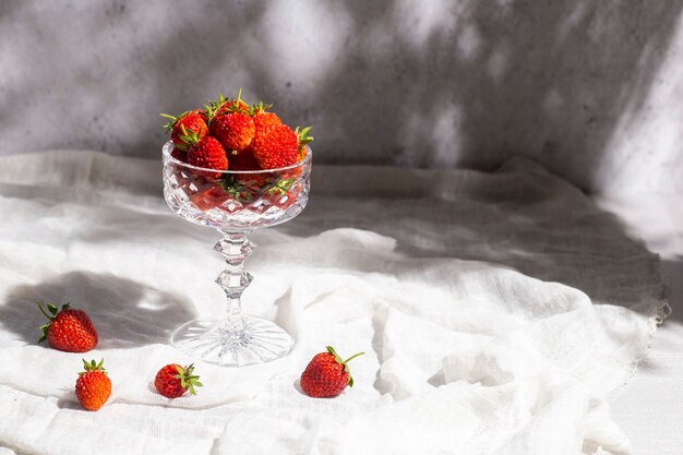 Frische rote Erdbeeren in einem Glas auf einem Tisch auf konkretem Hintergrund.