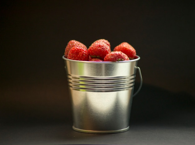 Frische rote Erdbeeren in metallischem Eimer auf schwarzer Hintergrundnahaufnahme. Rote Sommerbeeren. Leckeres und frisches Lebensmittelkonzept. Frische Sommerbeeren