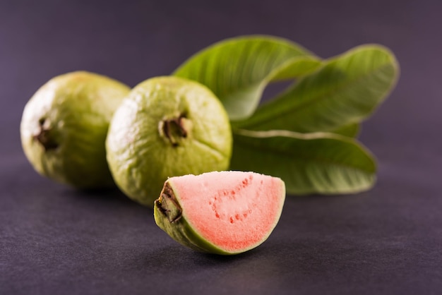 Frische rote Guavenfrucht, auch bekannt als Amrood in Hindi und Peru in Marathi, serviert in einem Korb als Ganzes oder in Scheiben auf buntem Hintergrund. Selektiver Fokus