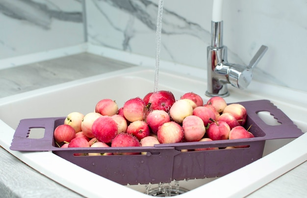 Frische rote Äpfel in der Spüle, Nahaufnahme. Äpfel in einem Sieb, unter fließendem Wasser gewaschen.