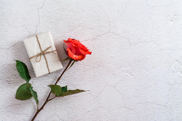 Frische rote Rose und ecowrapped Geschenk auf grauem Beschaffenheitshintergrund Draufsicht