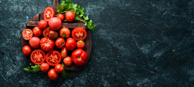 Frische rote Tomaten auf schwarzem Steinhintergrund Grüne Ansicht von oben Freier Platz für Ihren Text