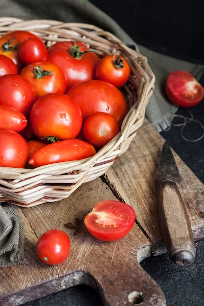 Frische rote Tomaten im Weidenkorb auf schwarzem Hintergrund.