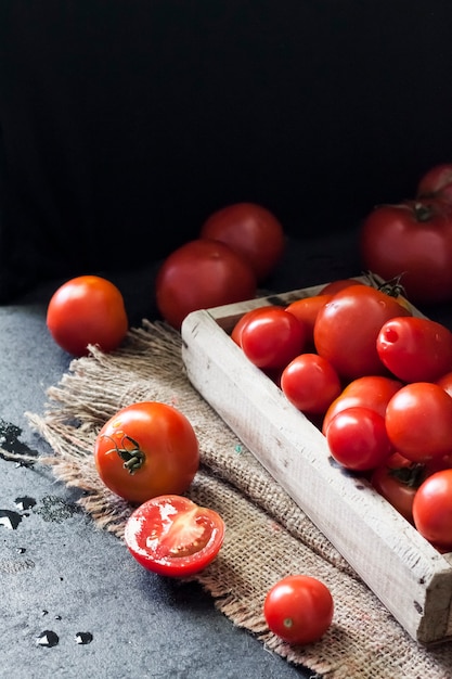 Frische rote Tomaten in Holzkiste auf schwarzem Hintergrund.