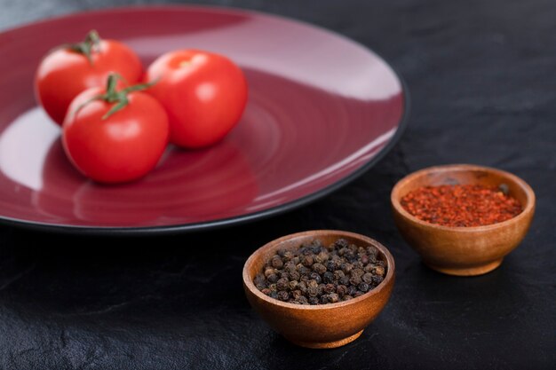 Frische rote Tomaten mit Pfefferkörnern und Pulver auf schwarzen Tisch gelegt.