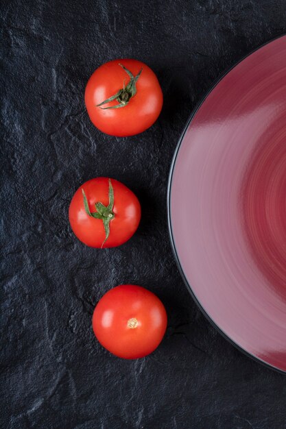 Frische rote Tomaten mit Teller auf schwarzem Tisch.