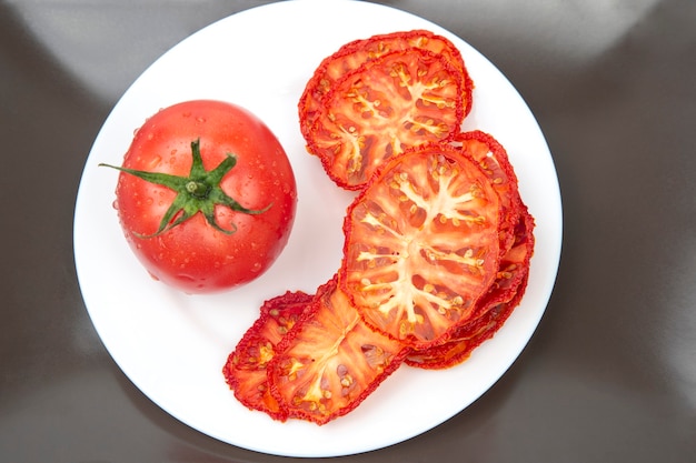 Frische rote Tomaten und getrocknete Tomatenscheiben auf einem Teller. Vitamin Gemüselebensmittel