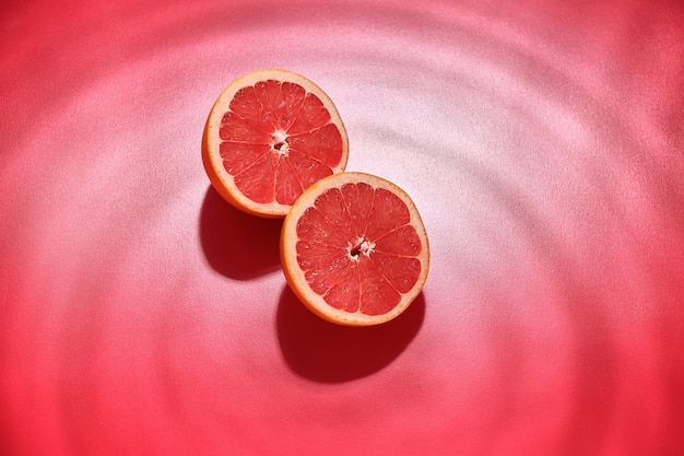 Frische saftige Grapefruit halbiert auf rotem Hintergrund mit der Wirkung von Wasserwellen. Frische Sommerfrüchte.