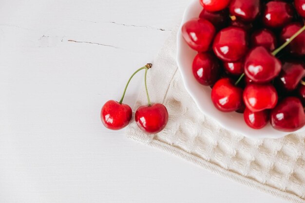 Frische saftige rote Kirschen in einem weißen Teller auf weißem Holzhintergrund