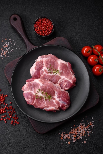 Frische saftige Schweinesteaks mit Salzgewürzen und Kräutern auf dunklem Betongrund