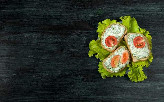 Frische Sandwiche mit Gemüse auf einem dunklen Brett auf einer strukturierten Oberfläche.