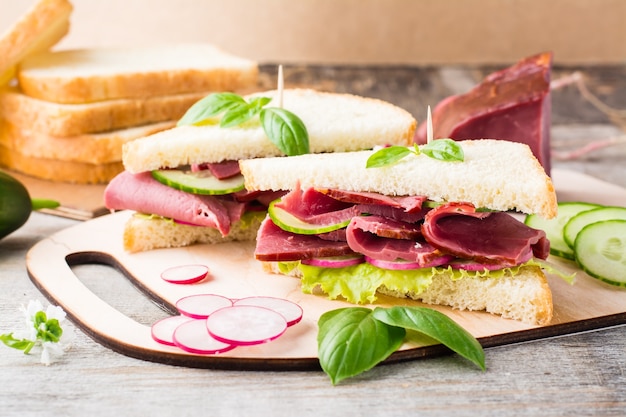 Frische Sandwiches mit Pastrami und Gemüse auf einem Schneidebrett. Amerikanischer Imbiss. Rustikaler Stil.