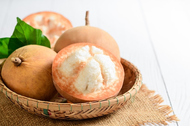 Frische Santol-Früchte auf Bambuskorb und auf weißem Holzhintergrund