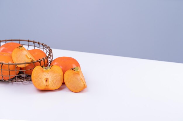 Frische schöne geschnittene süße Persimmon-Kaki isoliert auf weißem Küchentisch mit graublauem Hintergrund Chinesisches Mondneujahr-Designkonzept aus nächster Nähe