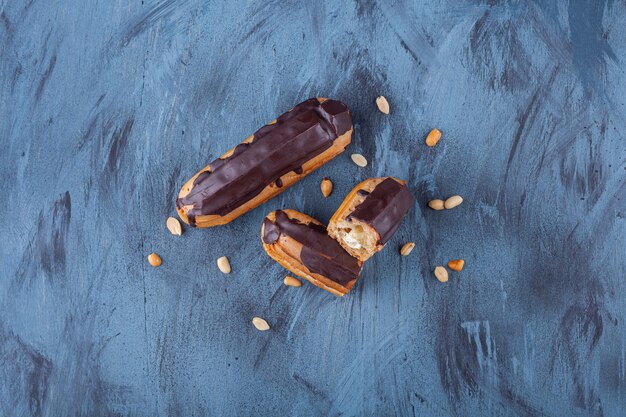 Frische Schokoladen-Eclairs und Erdnüsse auf Blau gelegt.