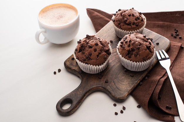 Frische Schokoladenmuffins auf Holzschneidebrett in der Nähe von Serviettengabel und Kaffee