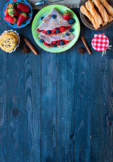 Frische selbst gemachte Krepps dienten auf einer Platte mit Erdbeeren und Blaubeeren auf einem dunklen hölzernen Hintergrund