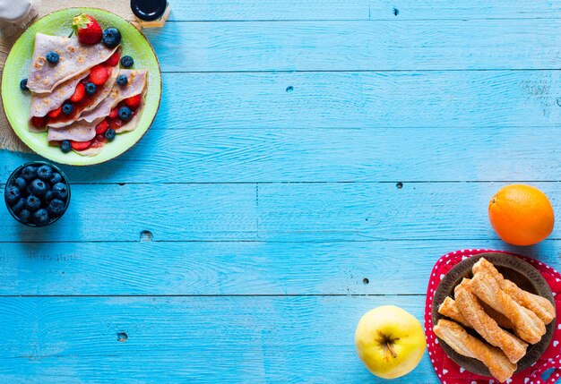 Frische selbst gemachte Krepps dienten auf einer Platte mit Erdbeeren und Blaubeeren auf einem freien Raum des hellblauen hölzernen Hintergrundes für Text.