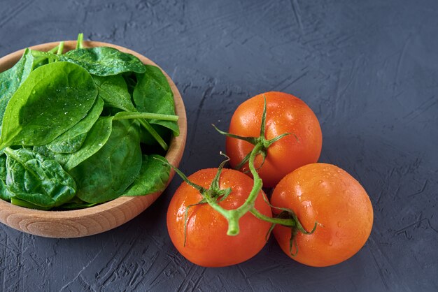 Frische Spinatblätter in der Holzschale und in der Tomate auf einem dunklen Hintergrund. Bio-Lebensmittel