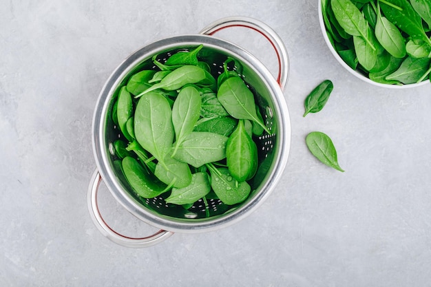 Frische spinatblätter roher spinat in einem sieb für vegetarischen oder veganen salat oder smoothie auf grauem betonhintergrund draufsicht kopierraum