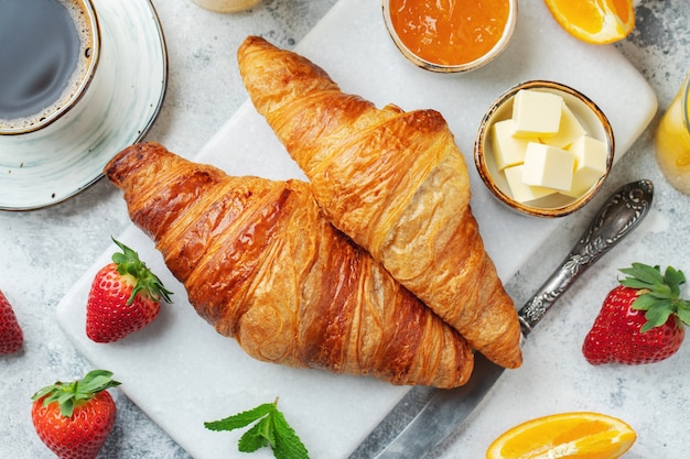 Frische süße Croissants mit Butter und Orangenmarmelade zum Frühstück. Kontinentales Frühstück auf einem weißen Betontisch. Ansicht von oben. Flach liegen.