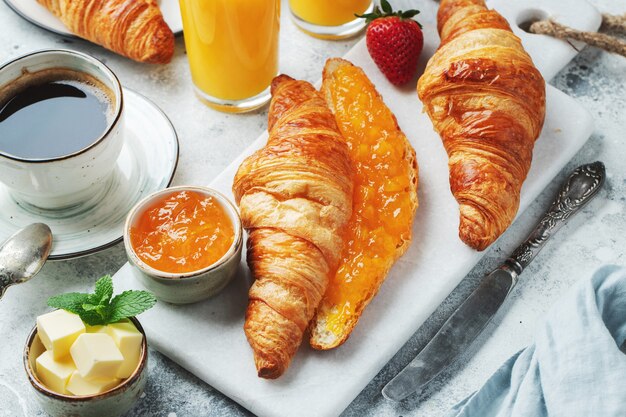 Frische süße Croissants mit Butter und Orangenmarmelade zum Frühstück. Kontinentales Frühstück auf einem weißen Betontisch.