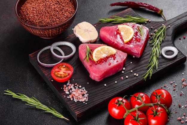 Frische Thunfischfiletsteaks mit Gewürzen und Kräutern auf einem schwarzen Hintergrund