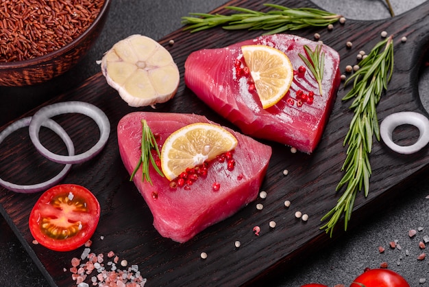 Frische Thunfischfiletsteaks mit Gewürzen und Kräutern auf einem schwarzen Hintergrund