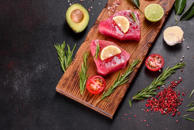 Frische Thunfischfiletsteaks mit Gewürzen und Kräutern auf schwarzer Oberfläche. Thunfisch zum Backen vorbereiten