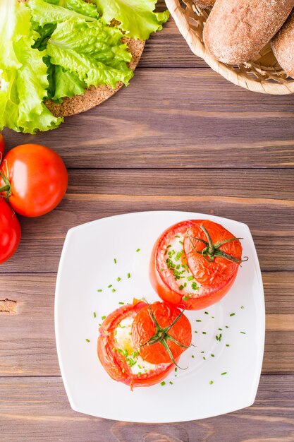 Frische Tomaten backten mit dem Käse und Ei, die mit Frühlingszwiebeln auf einer Platte auf einem Holztisch besprüht wurden.