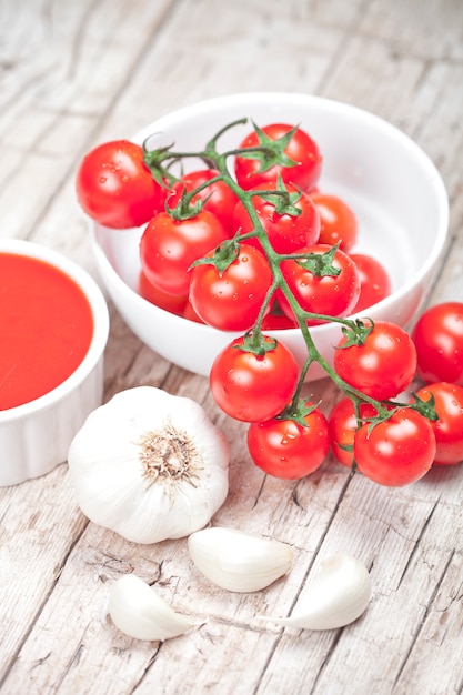 Frische Tomaten in der weißen Schüssel, in der Soße und im rohen Knoblauch auf rustikalem Holztisch.