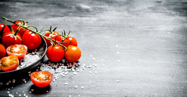 Frische Tomaten mit grobem Salz. Auf schwarzem rustikalem Tisch.