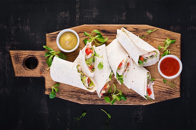 Frische Tortilla Wraps mit Huhn und frischem Gemüse auf Holzbrett.