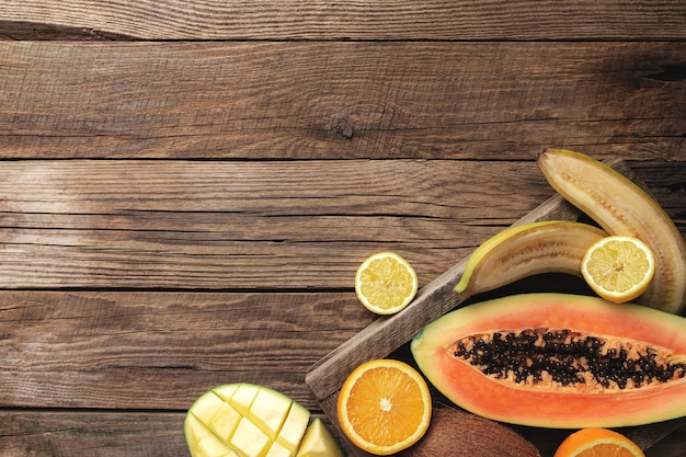 Frische tropische Früchte in einer Holzkiste auf einem Holztisch. Papaya, Orange, Banane, Kokosnuss, Mango, Kiwi und Zitrone