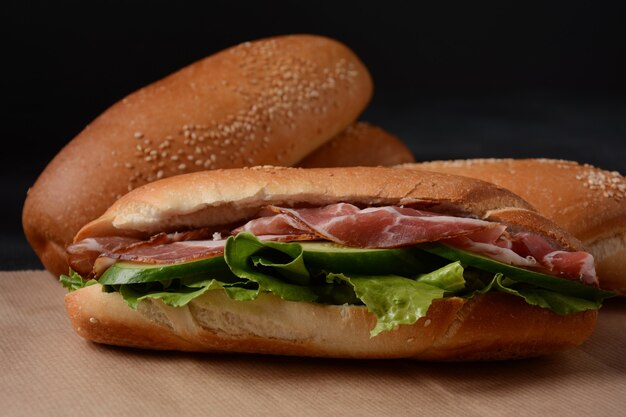 Frische U-Boot-Sandwiches mit Speck, Käse, Tomaten, Salat, Gurken und Zwiebeln auf dunklem Hintergrund