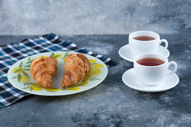 Frische und leckere Croissants mit zwei Tassen heißem Tee auf Steintisch