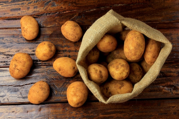 Frische und rohe Kartoffeln geerntet von der Plantage und in eine rustikale Tasche auf Holztisch gelegt