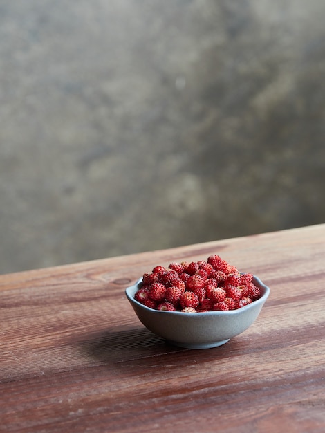 Foto frische walderdbeeren in einer kleinen schüssel auf einem holztisch. fragaria vesca