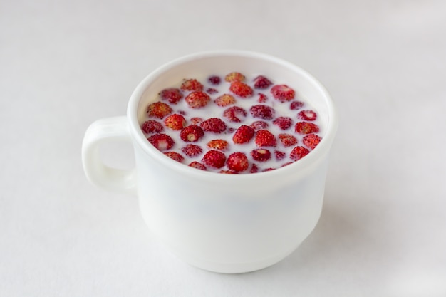 Frische Walderdbeeren mit Milch in einem weißen Becher.