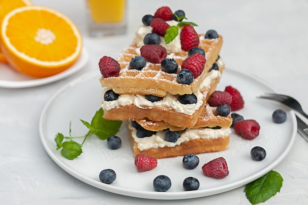 Frische Wiener oder belgische Waffeln auf einem Teller mit frischen Himbeeren und Heidelbeeren und Schlagsahne