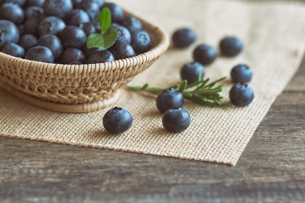 Frische wilde Blaubeeren im hölzernen Korb auf Sack setzten an Holztisch mit Kopienraum.