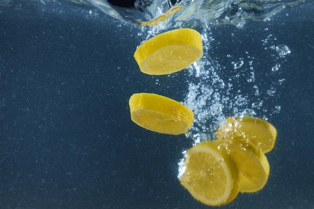 Frische Zitronenscheiben, die in Wasser fallen, mit Spritzen, die über dunkelblauen Hintergründen isoliert sind