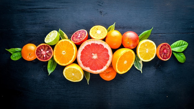 Frische Zitrusfrüchte. Zitrone, Orange, Mandarine, Limette. Auf schwarzem Hintergrund aus Holz. Ansicht von oben.