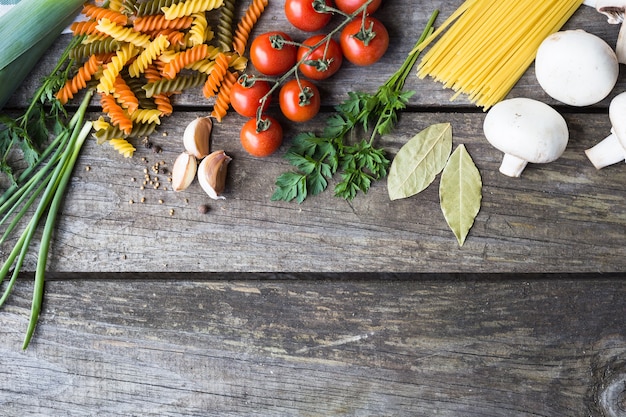 Frische Zutaten zum Kochen von Nudeln, Tomaten und Gewürzen über Holztischhintergrund mit Kopierraum