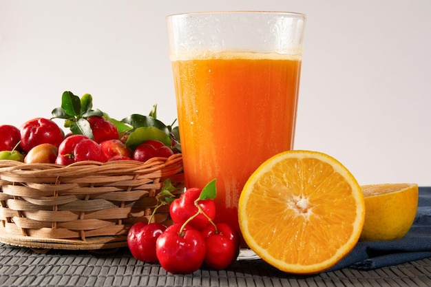 Frischer Acerola-Saft in einem Glasbecher in einer Bambusmatte mit geschnittenen Orangen und Acerolafrüchten