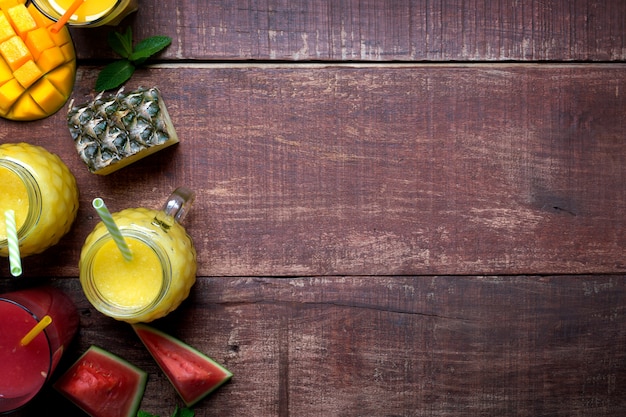 Frischer Ananas-Mango-Smoothie in Gläsern mit Früchten auf einem rustikalen hölzernen Hintergrund mit Kopienraum auf der rechten Seite