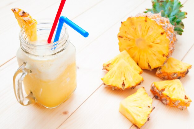 Frischer Ananas Smoothie mit Ananasscheibe auf Holztisch