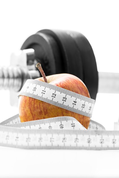 Frischer Apfel, eingewickelt in ein Maßband mit einem Gewicht im Fitnessstudio. Gewichtsverlust, Gesundheit, Ernährung und Fitness-Konzept.