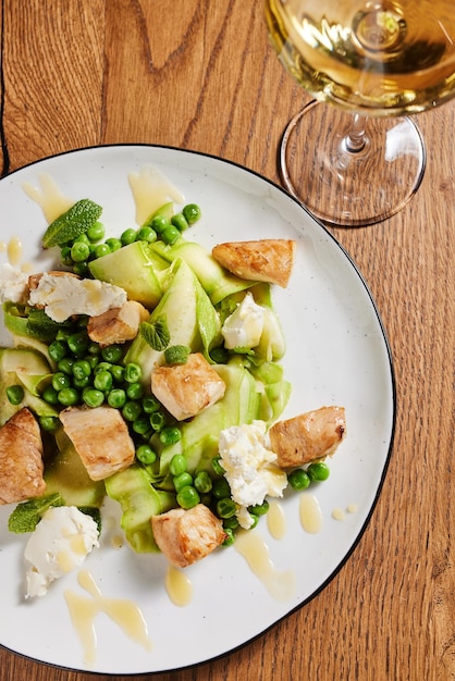 frischer appetitlicher Salat aus Hähnchen, Erbsen, Feta-Käse und Gurken auf einem Holztisch